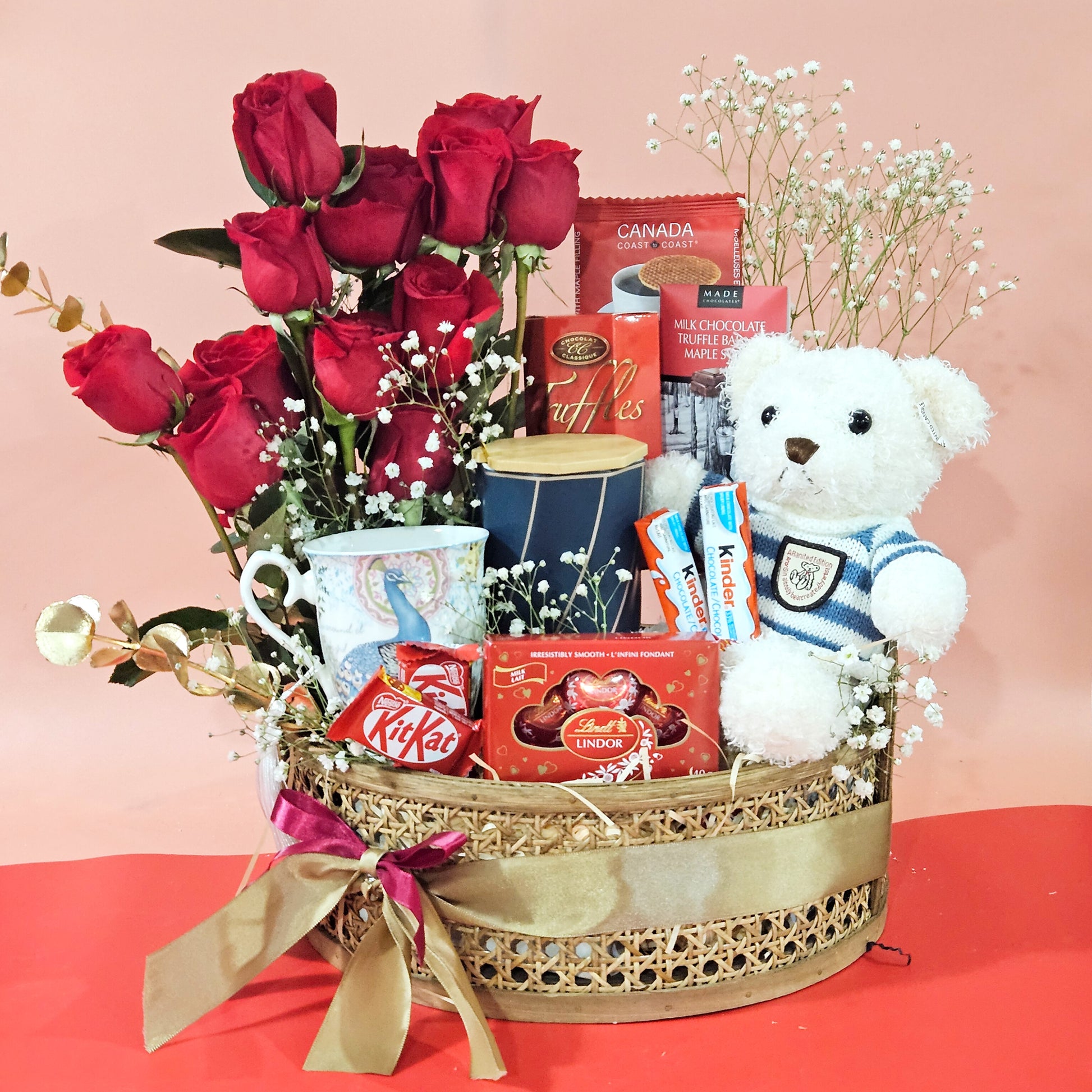 A gift basket containing a fresh rose arrangement, coffee mugs, gourmet chocolate, and a teddy bear.