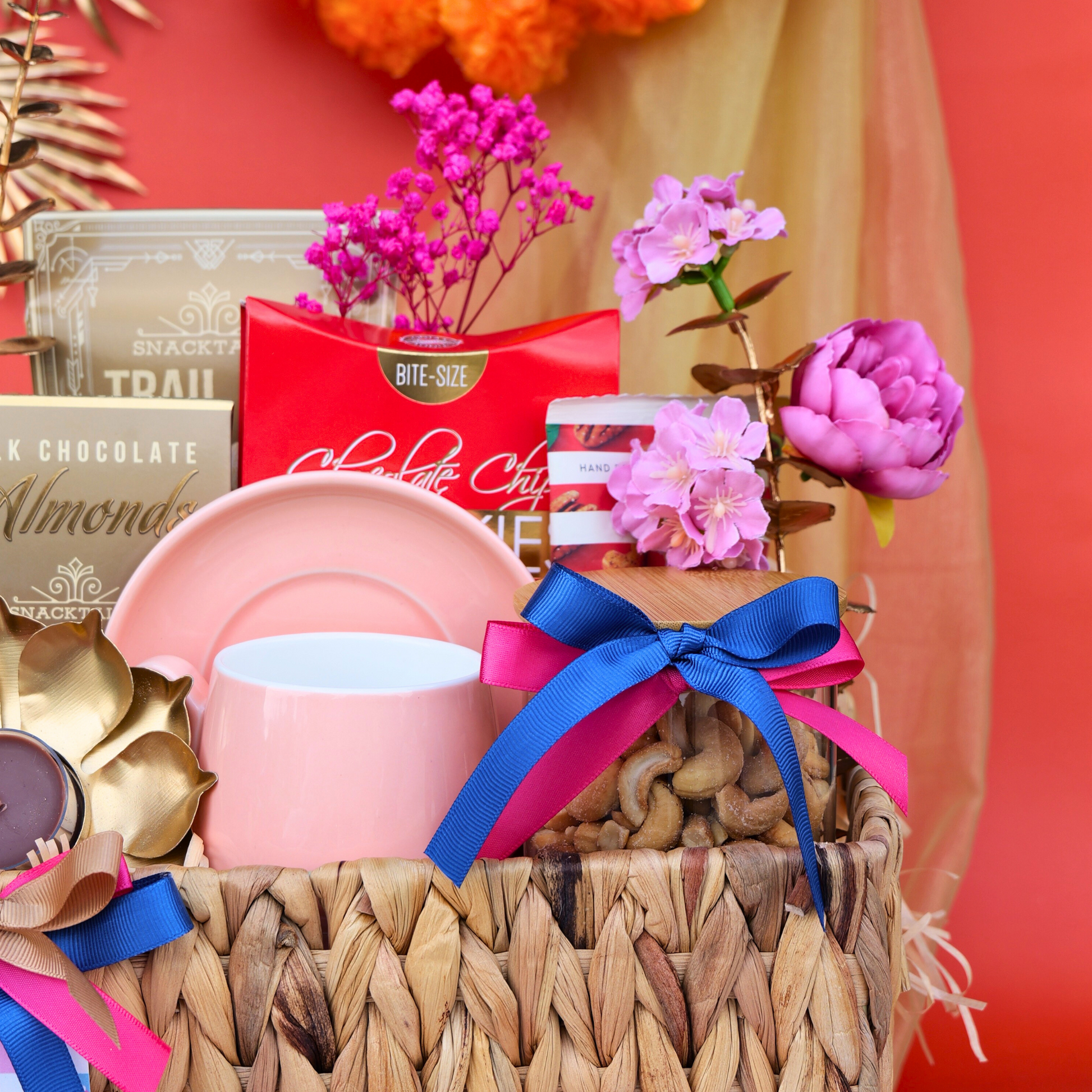 Gift basket with pink mug, snacks, and flowers on a red background
