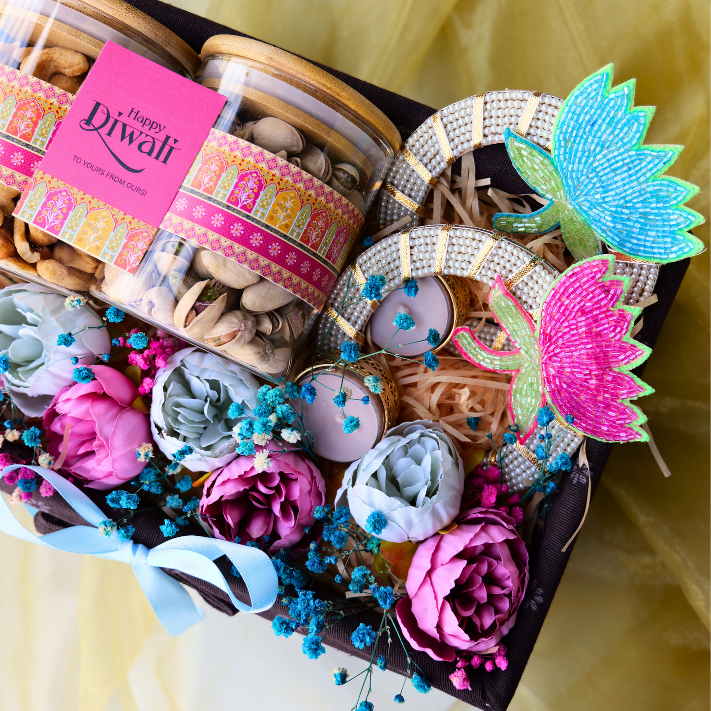 Decorative gift box with flowers, jewelry, and Diwali-themed items on a yellow background