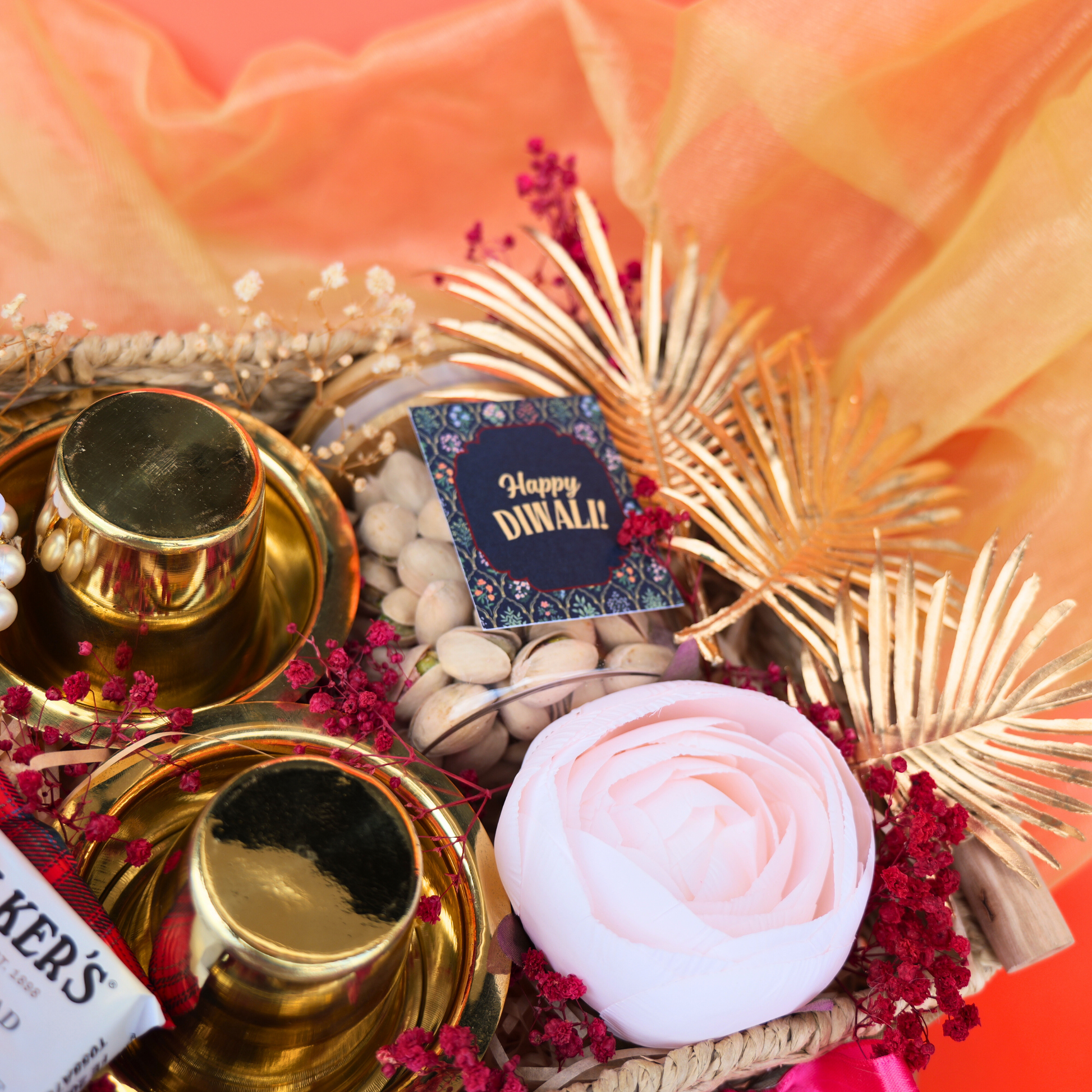 Decorative Diwali gift basket with candles, flowers, and a card on an orange fabric background.