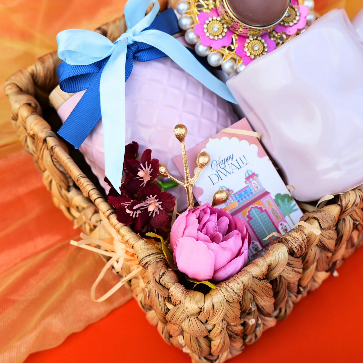 Decorative basket with pink fabric, flowers, and a card on an orange background