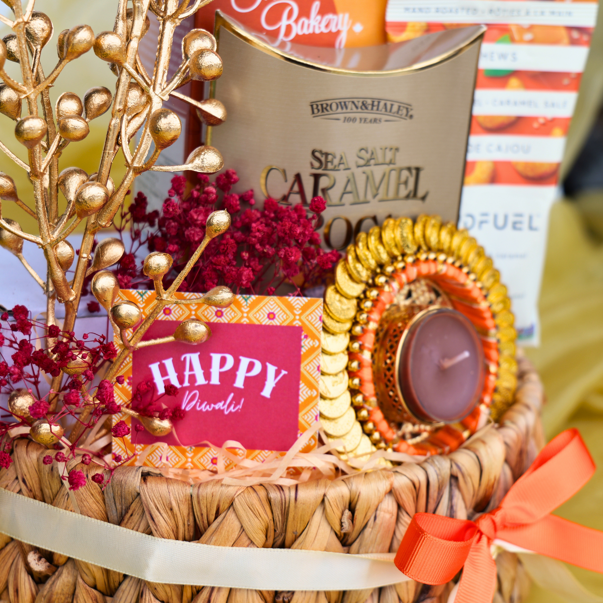 Decorative gift basket with candles, flowers, and a 'Happy Diwali!' card on a blurred background.