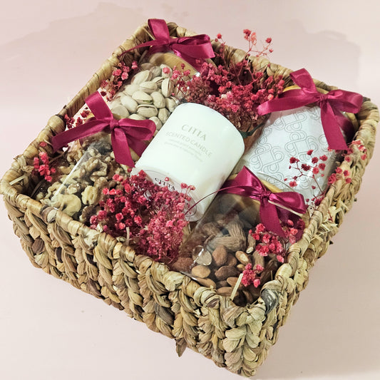 Gift basket with candles, flowers, and snacks on a light pink background