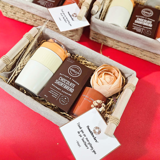 Wicker basket with wooden handle containing a white and orange item, presumably a soy wax candle, and a brown item, possibly a cookie box, with a red background.