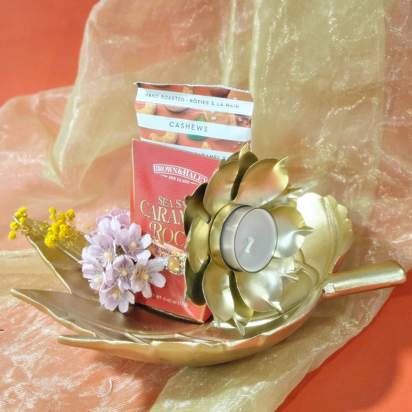 Decorative tray with a candle, flowers, and a cashew package on a textured surface.