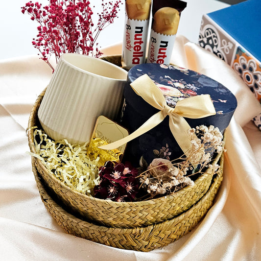 A Navy blue momos gift basket containing a vintage tea cup, a lemon yellow vase, and a gold acrylic plating with a Ramadan Kareem print. The basket is adorned with decorative flowers and ribbons.