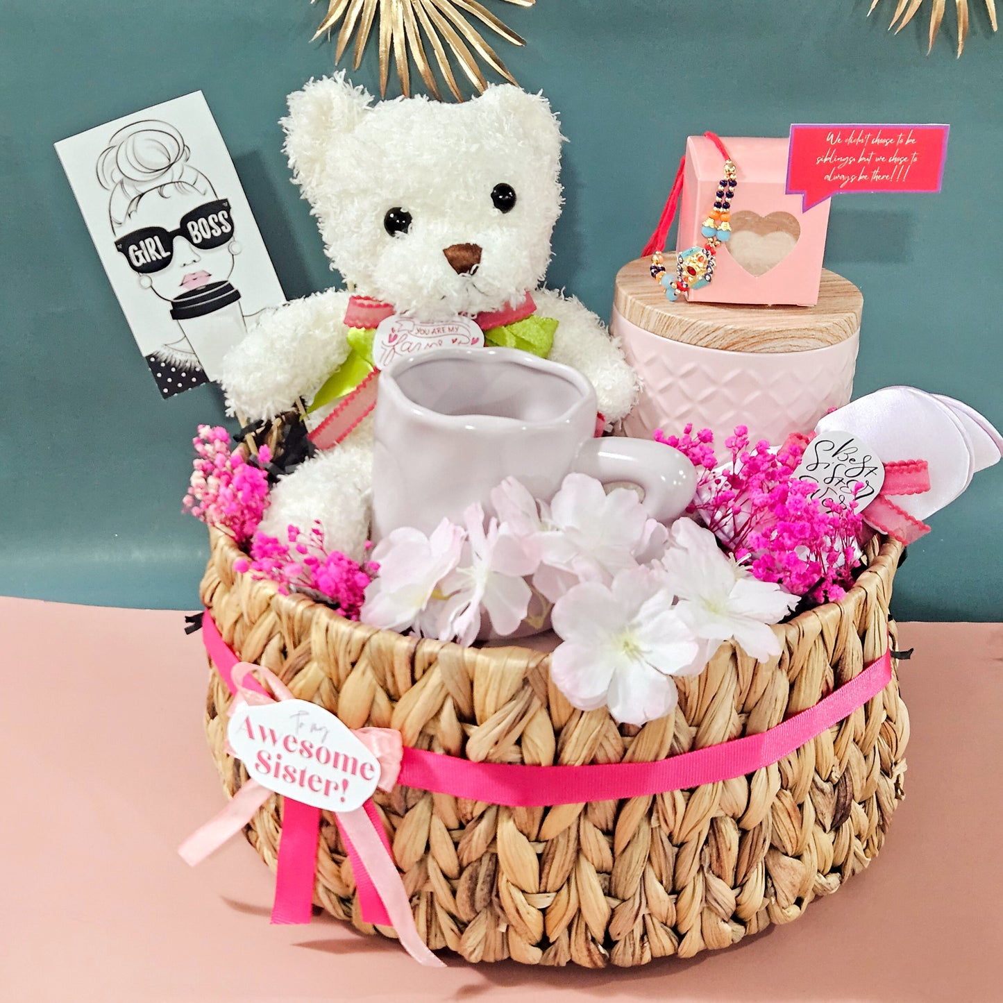 Gift basket with teddy bear, mug, and flowers on a pink surface with a teal background