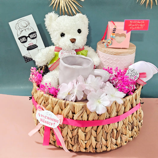 Gift basket with teddy bear, mug, and flowers on a pink surface with a teal background