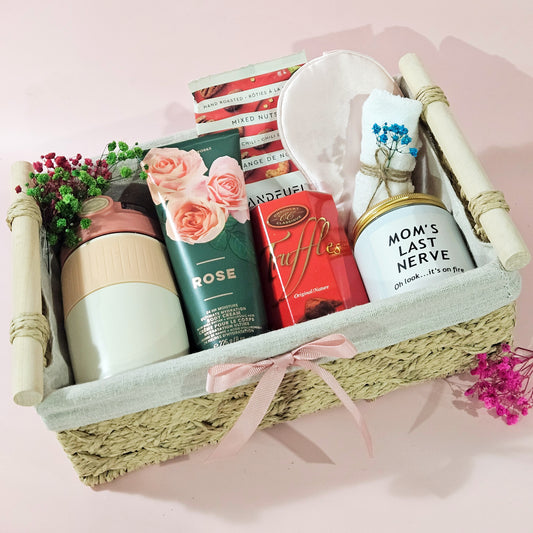 Gift basket with various items including a mug, snacks, and a small plant on a pink background